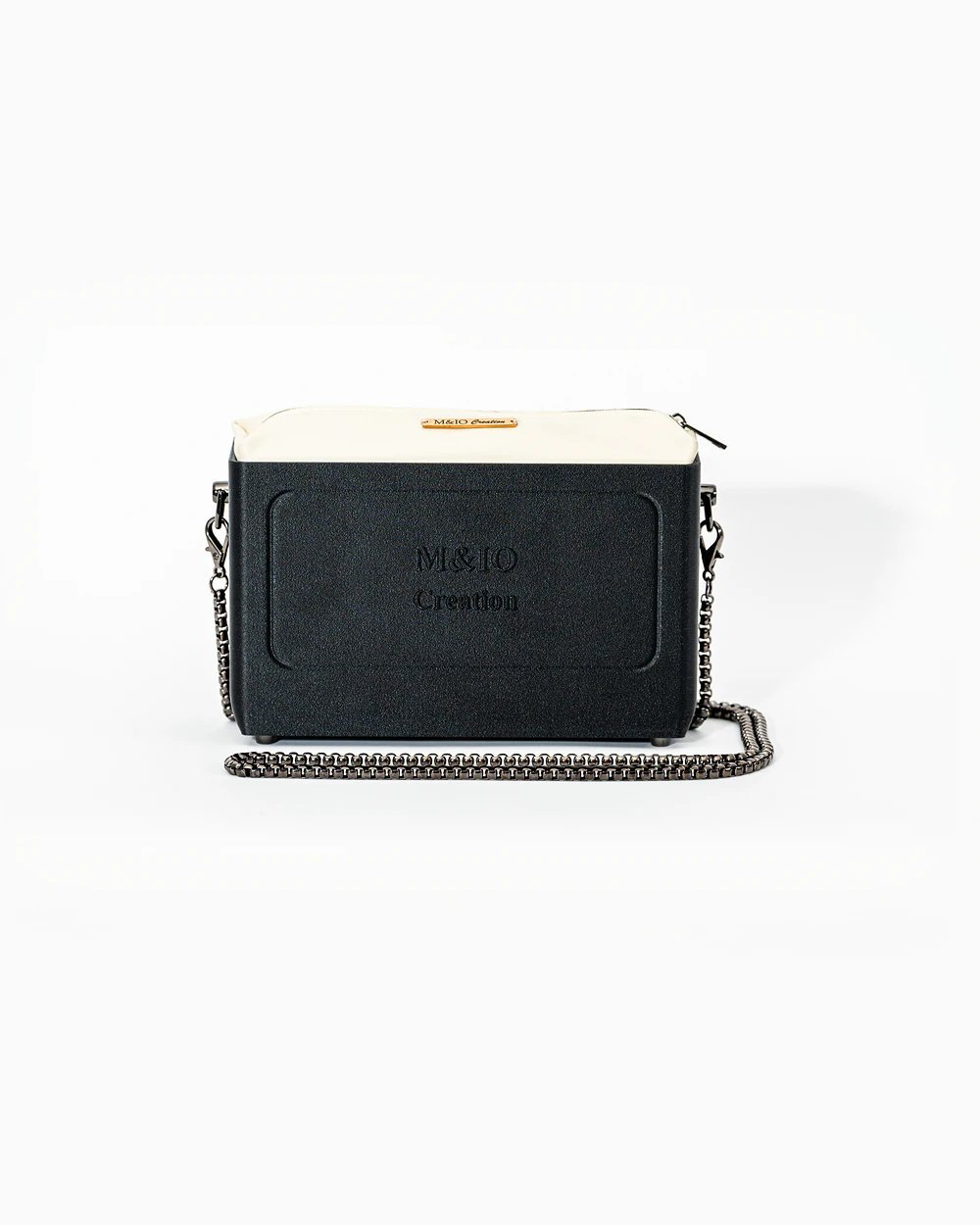 Borsa M&IO 01 di tre quarti: scocca black stone opaca con la scritta M&IO Creation in rilievo sul fronte, pochette bianco panna che sporge dal bordo superiore, catena in metallo canna di fucile.