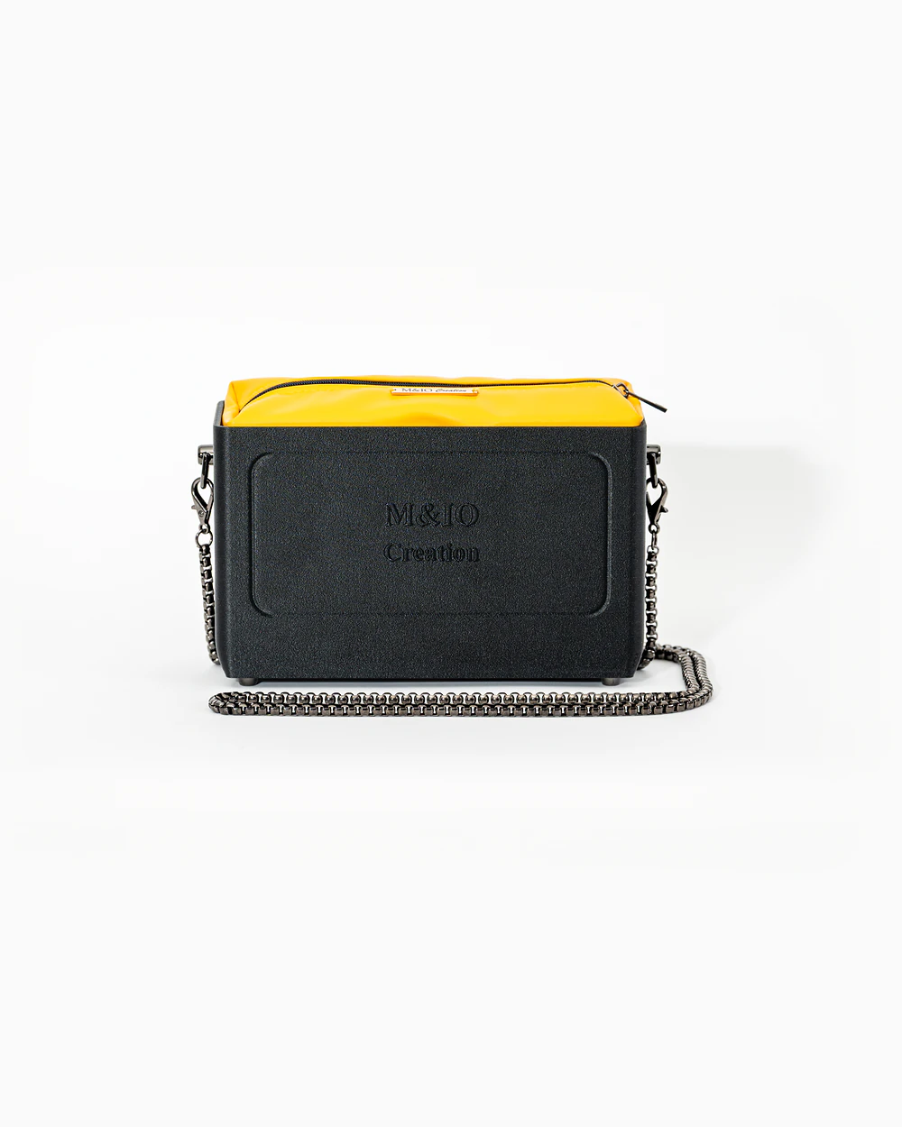 Borsa M&IO 01 di tre quarti: scocca black stone opaca con la scritta M&IO Creation in rilievo sul fronte, pochette giallo che sporge dal bordo superiore, catena in metallo canna di fucile.