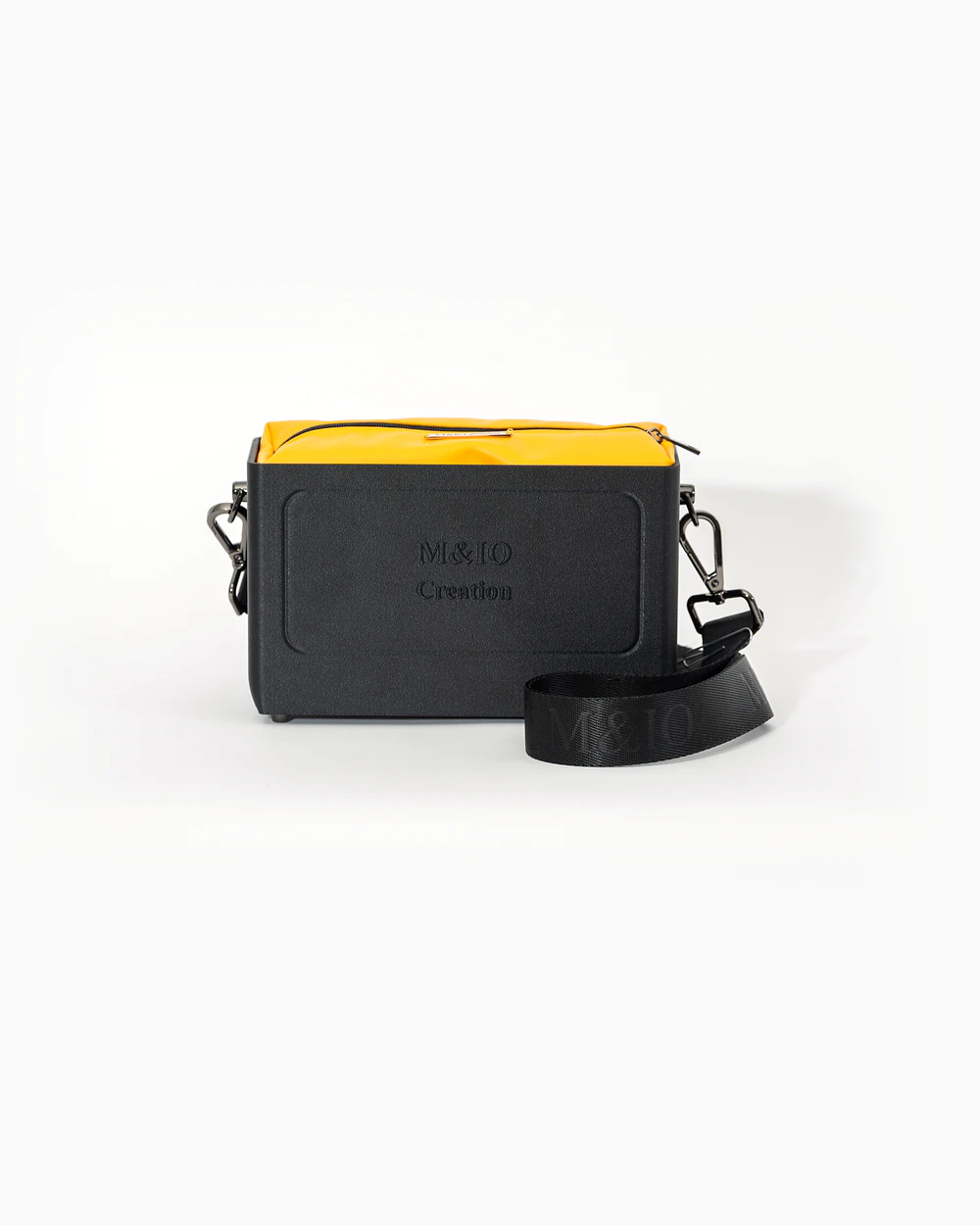 Borsa M&IO 01 di tre quarti: scocca black stone opaca con la scritta M&IO Creation in rilievo sul fronte, pochette giallo che sporge dal bordo superiore, cinghia in tessuto nero con logo M&IO ripetuto.