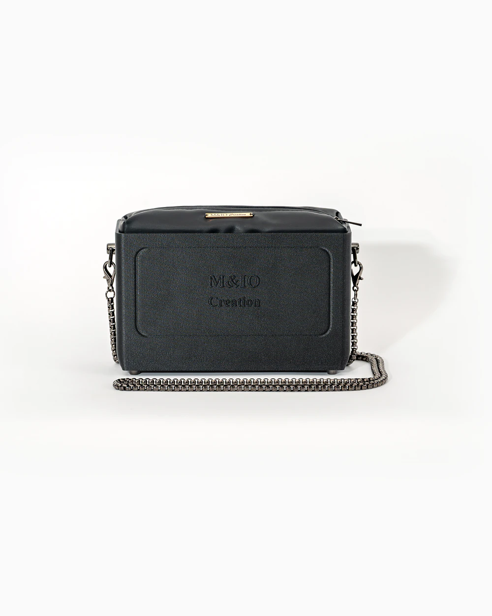 Borsa M&IO 01 di tre quarti: scocca black stone opaca con la scritta M&IO Creation in rilievo sul fronte, pochette nero che sporge dal bordo superiore, catena in metallo canna di fucile.