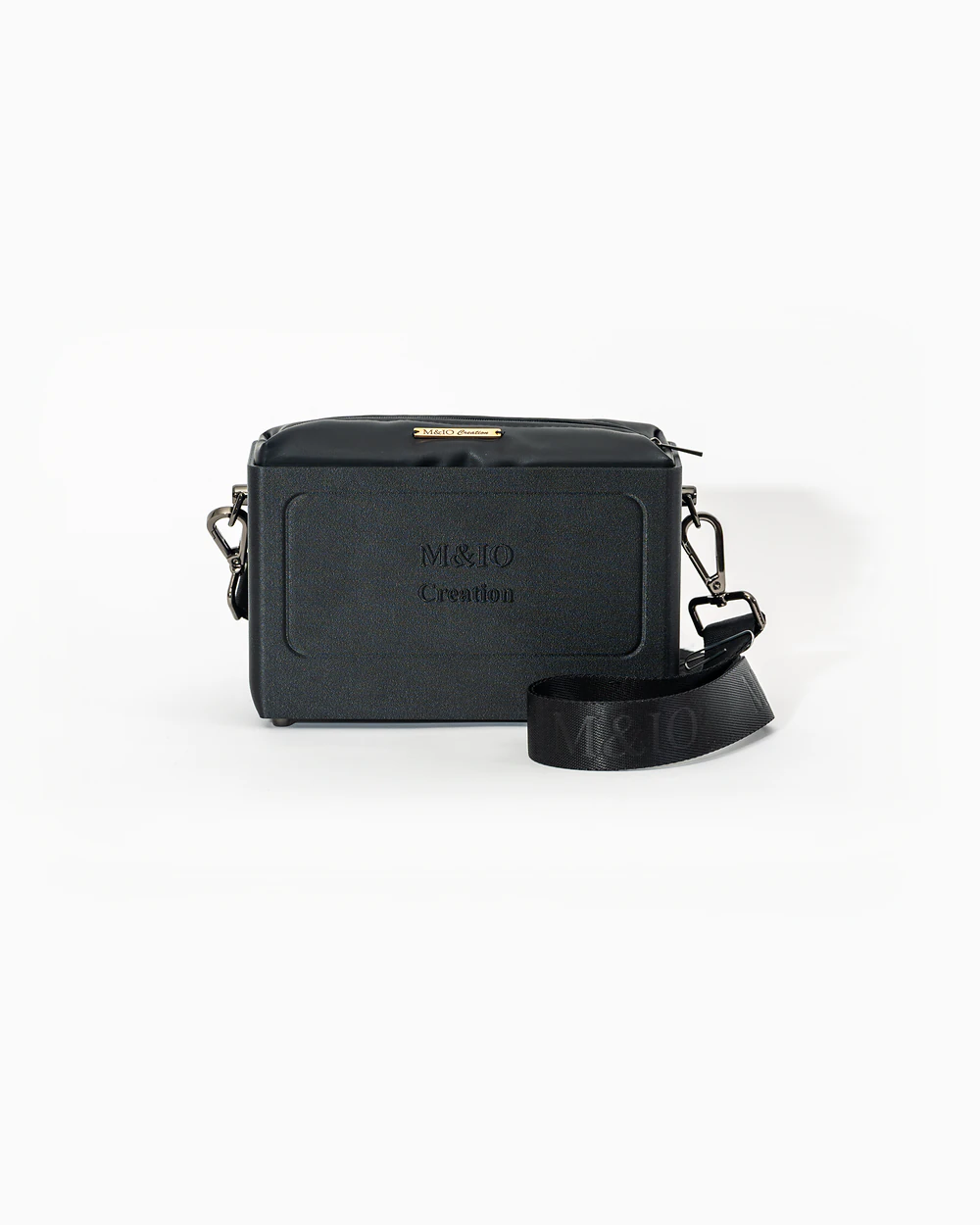 Borsa M&IO 01 di tre quarti: scocca black stone opaca con la scritta M&IO Creation in rilievo sul fronte, pochette nero che sporge dal bordo superiore, cinghia in tessuto nero con logo M&IO ripetuto.