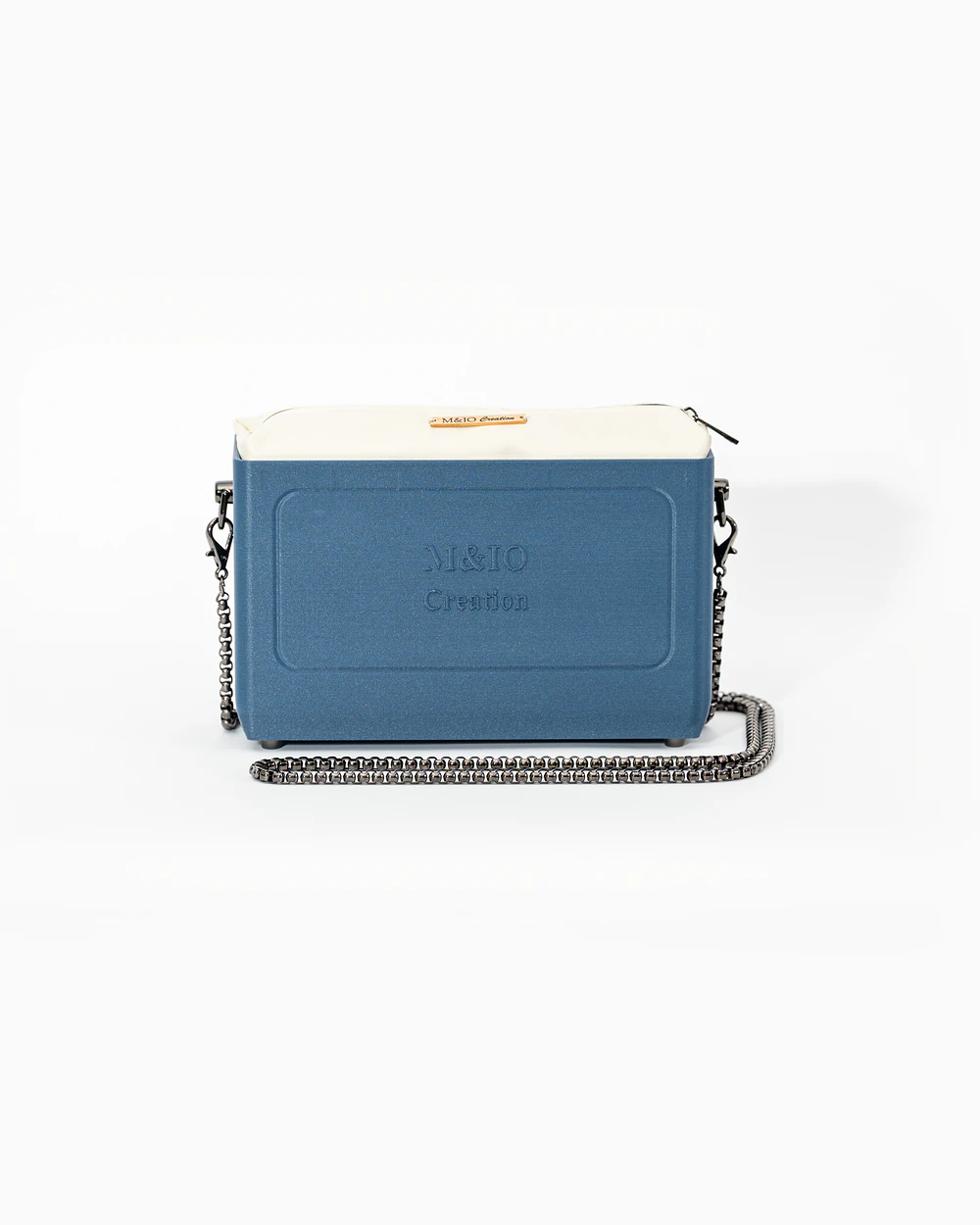 Borsa M&IO 01 di tre quarti: scocca blu portofino opaca con la scritta M&IO Creation in rilievo sul fronte, pochette bianco panna che sporge dal bordo superiore, catena in metallo canna di fucile.