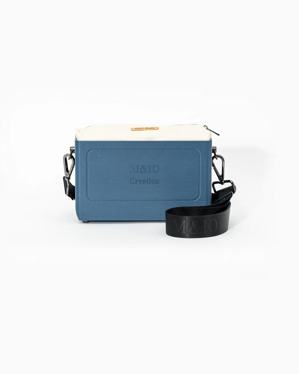 Borsa M&IO 01 di tre quarti: scocca blu portofino opaca con la scritta M&IO Creation in rilievo sul fronte, pochette bianco panna che sporge dal bordo superiore, cinghia in tessuto nero con logo M&IO ripetuto.