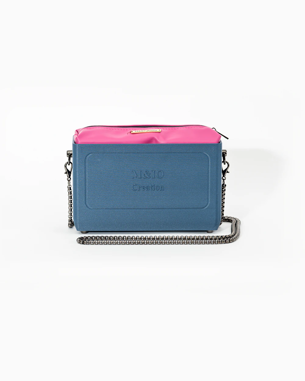 Borsa M&IO 01 di tre quarti: scocca blu portofino opaca con la scritta M&IO Creation in rilievo sul fronte, pochette fucsia che sporge dal bordo superiore, catena in metallo canna di fucile.