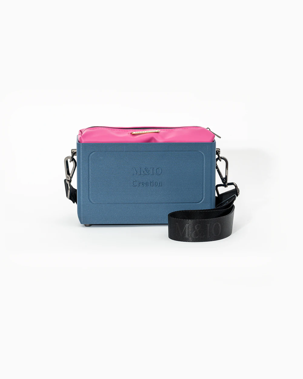 Borsa M&IO 01 di tre quarti: scocca blu portofino opaca con la scritta M&IO Creation in rilievo sul fronte, pochette fucsia che sporge dal bordo superiore, cinghia in tessuto nero con logo M&IO ripetuto.