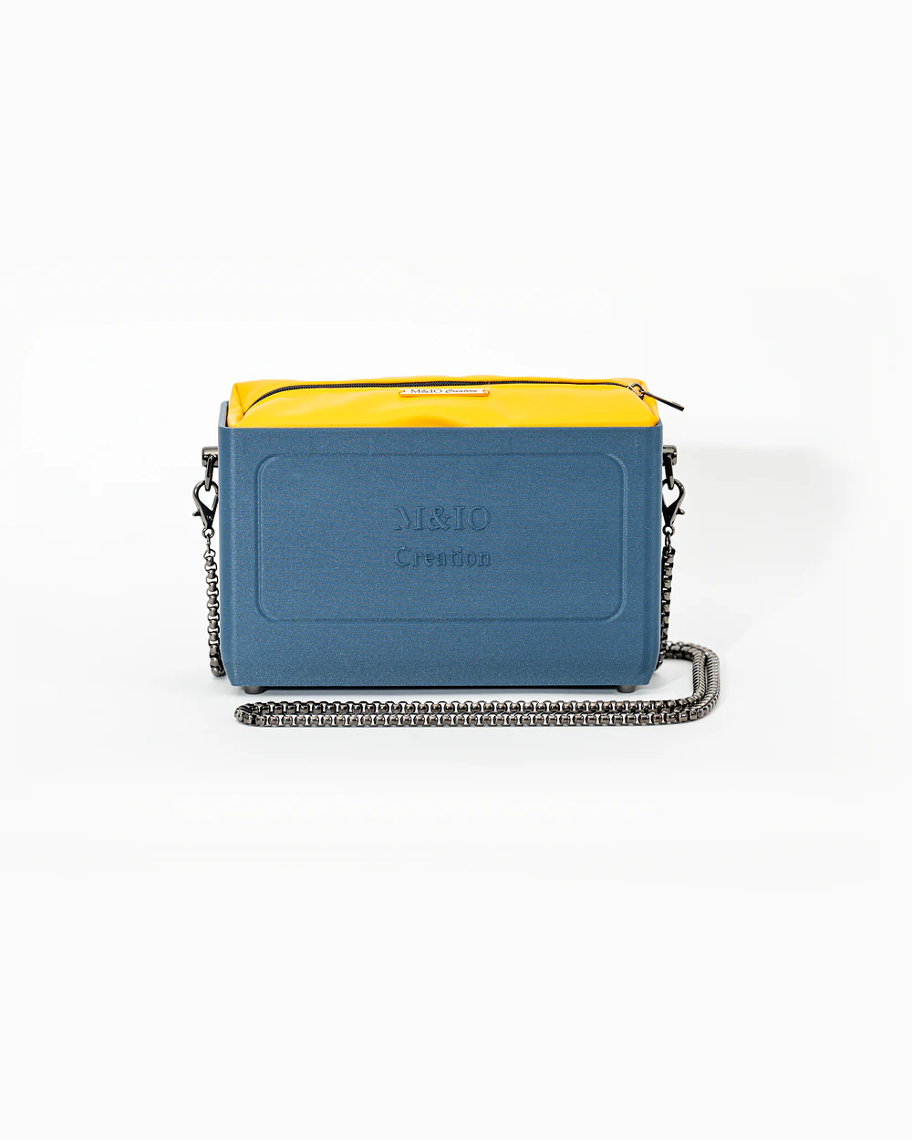 Borsa M&IO 01 di tre quarti: scocca blu portofino opaca con la scritta M&IO Creation in rilievo sul fronte, pochette giallo che sporge dal bordo superiore, catena in metallo canna di fucile.