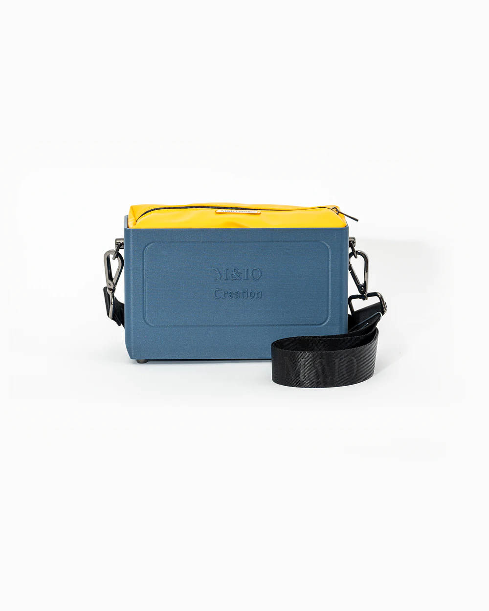 Borsa M&IO 01 di tre quarti: scocca blu portofino opaca con la scritta M&IO Creation in rilievo sul fronte, pochette giallo che sporge dal bordo superiore, cinghia in tessuto nero con logo M&IO ripetuto.