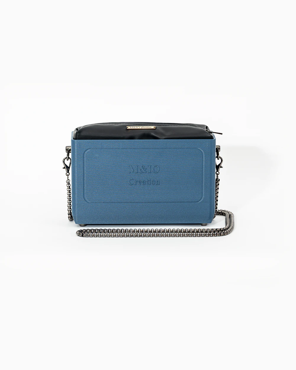 Borsa M&IO 01 di tre quarti: scocca blu portofino opaca con la scritta M&IO Creation in rilievo sul fronte, pochette nero che sporge dal bordo superiore, catena in metallo canna di fucile.