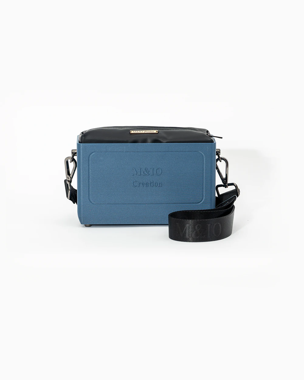 Borsa M&IO 01 di tre quarti: scocca blu portofino opaca con la scritta M&IO Creation in rilievo sul fronte, pochette nero che sporge dal bordo superiore, cinghia in tessuto nero con logo M&IO ripetuto.