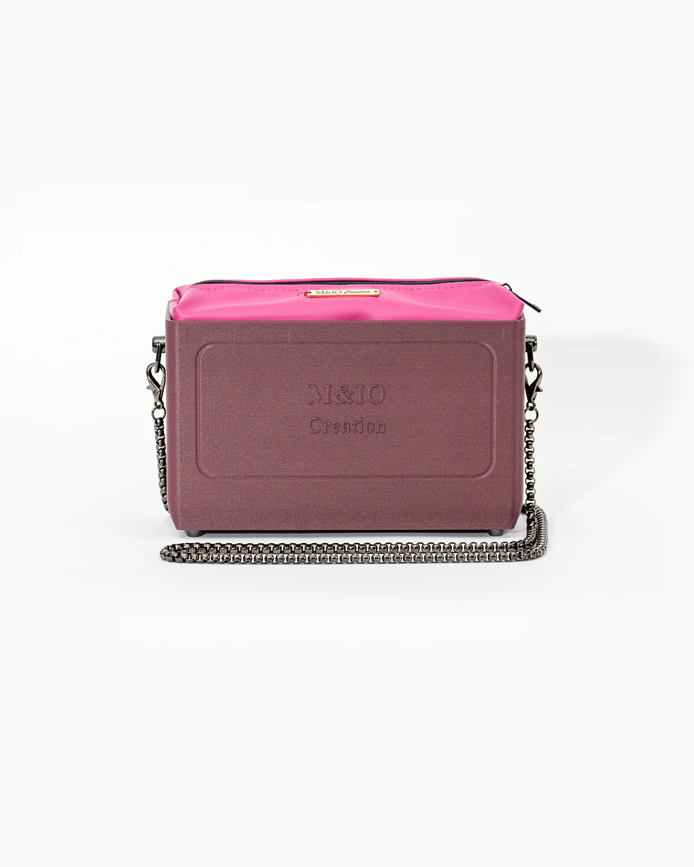 Borsa M&IO 01 di tre quarti: scocca rosso tropea opaca con la scritta M&IO Creation in rilievo sul fronte, pochette fucsia che sporge dal bordo superiore, catena in metallo canna di fucile.
