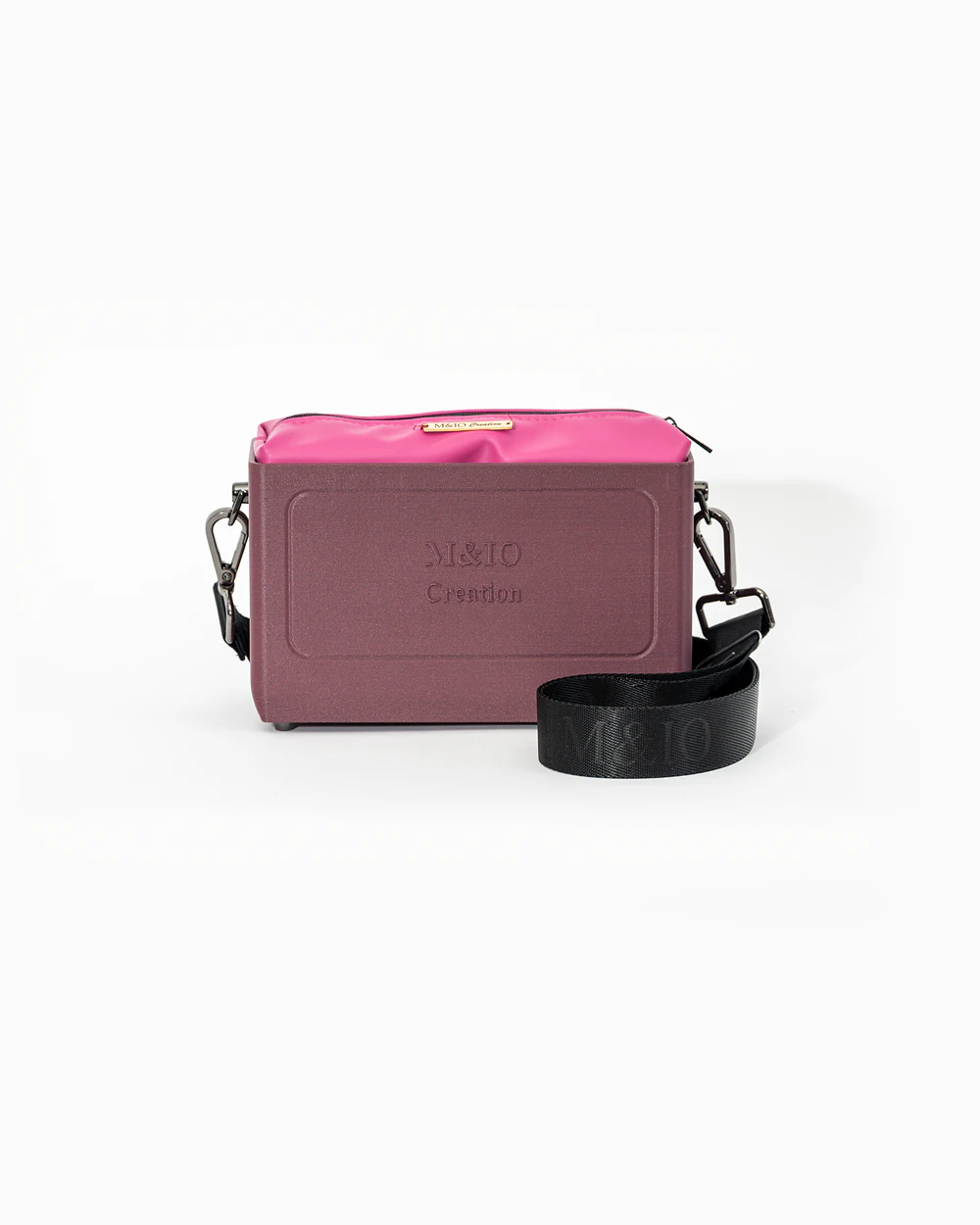 Borsa M&IO 01 di tre quarti: scocca rosso tropea opaca con la scritta M&IO Creation in rilievo sul fronte, pochette fucsia che sporge dal bordo superiore, cinghia in tessuto nero con logo M&IO ripetuto.