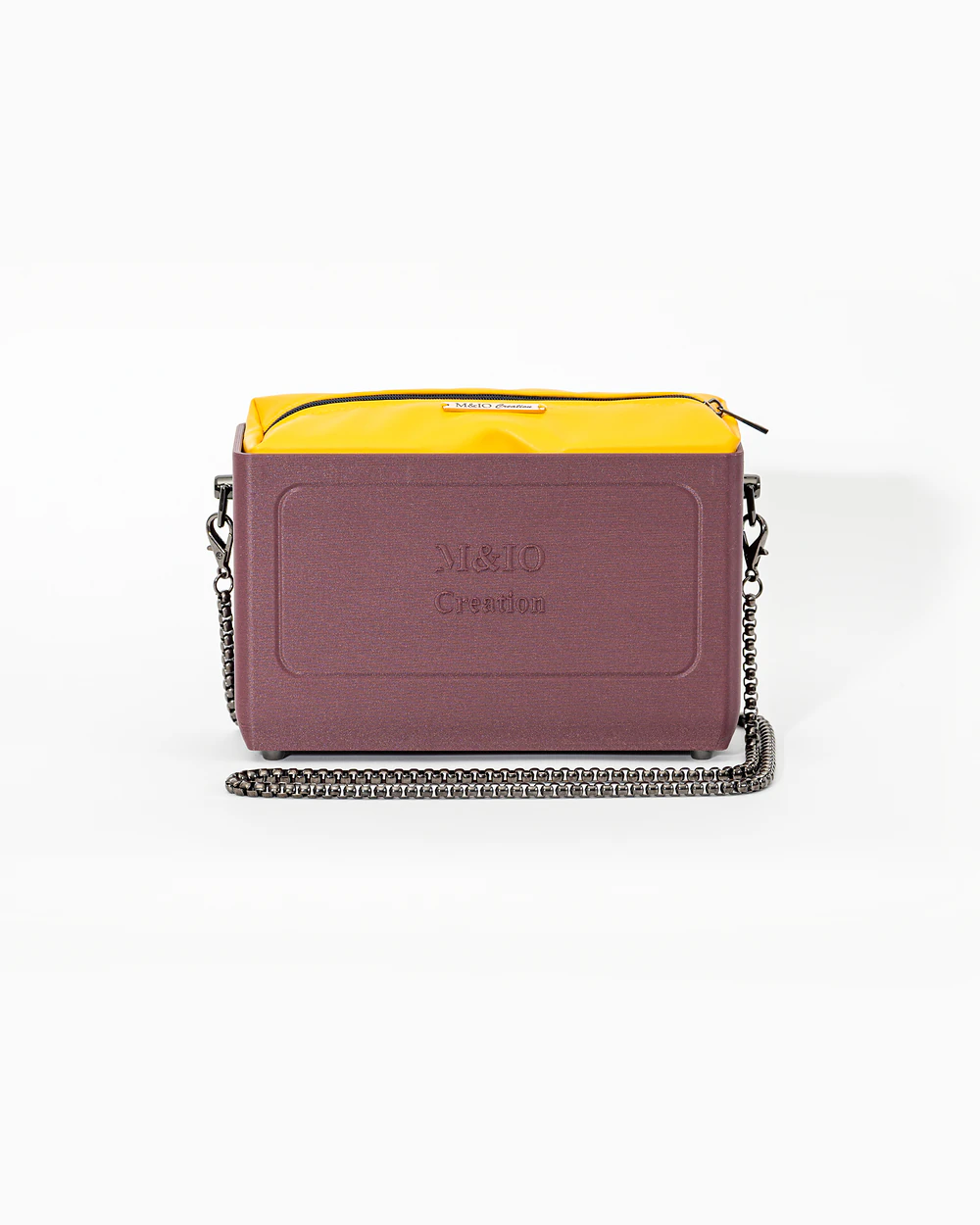 Borsa M&IO 01 di tre quarti: scocca rosso tropea opaca con la scritta M&IO Creation in rilievo sul fronte, pochette giallo che sporge dal bordo superiore, catena in metallo canna di fucile.