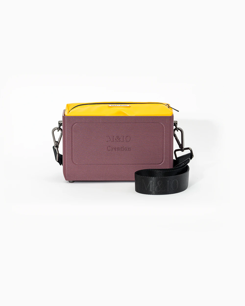Borsa M&IO 01 di tre quarti: scocca rosso tropea opaca con la scritta M&IO Creation in rilievo sul fronte, pochette giallo che sporge dal bordo superiore, cinghia in tessuto nero con logo M&IO ripetuto.