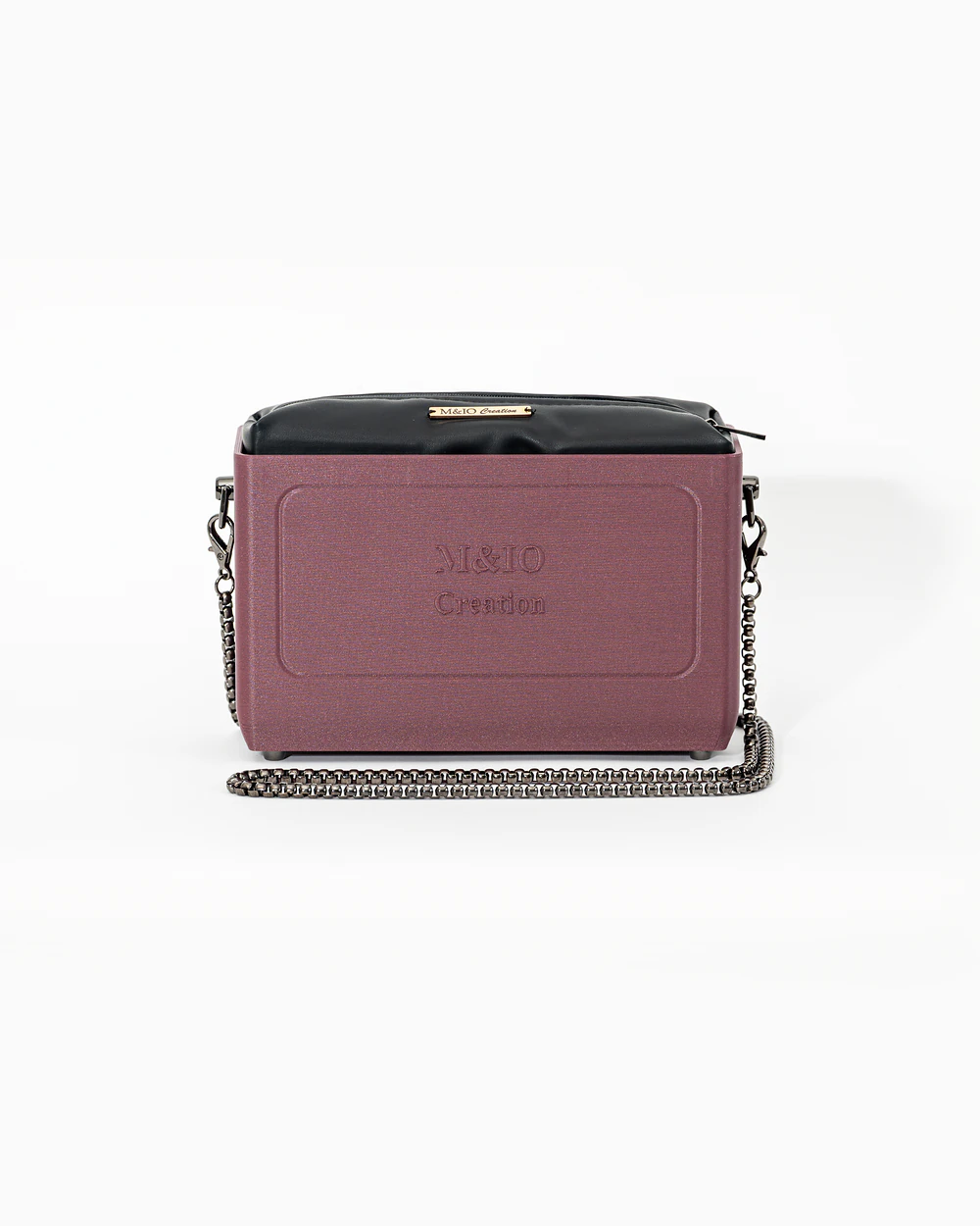 Borsa M&IO 01 di tre quarti: scocca rosso tropea opaca con la scritta M&IO Creation in rilievo sul fronte, pochette nero che sporge dal bordo superiore, catena in metallo canna di fucile.