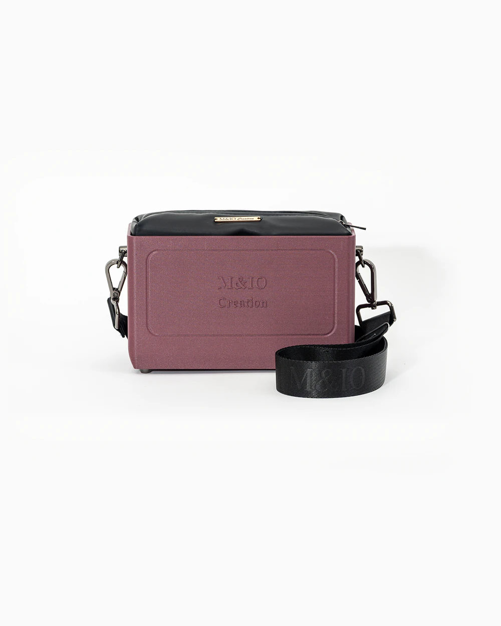 Borsa M&IO 01 di tre quarti: scocca rosso tropea opaca con la scritta M&IO Creation in rilievo sul fronte, pochette nero che sporge dal bordo superiore, cinghia in tessuto nero con logo M&IO ripetuto.