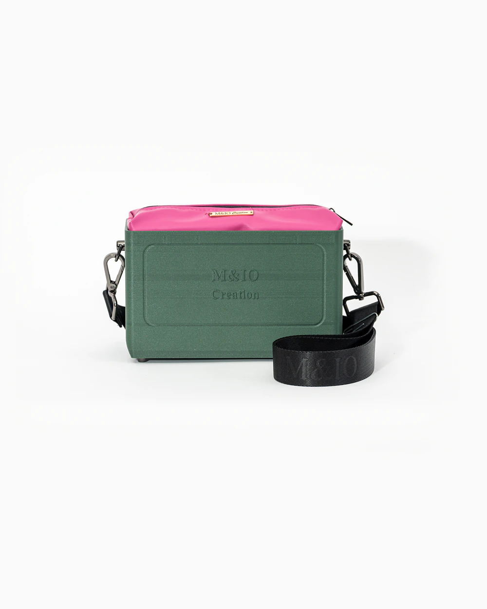 Borsa M&IO 01 di tre quarti: scocca ulivi di puglia opaca con la scritta M&IO Creation in rilievo sul fronte, pochette fucsia che sporge dal bordo superiore, cinghia in tessuto nero con logo M&IO ripetuto.