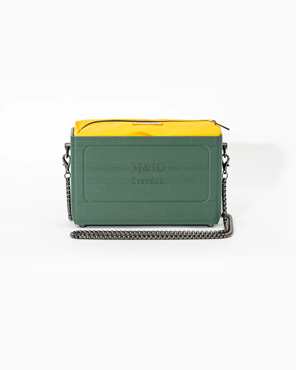 Borsa M&IO 01 di tre quarti: scocca ulivi di puglia opaca con la scritta M&IO Creation in rilievo sul fronte, pochette giallo che sporge dal bordo superiore, catena in metallo canna di fucile.