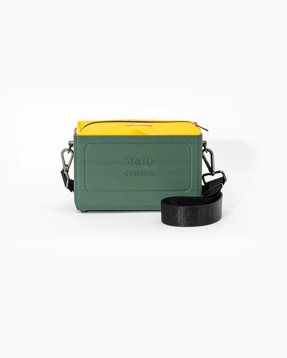 Borsa M&IO 01 di tre quarti: scocca ulivi di puglia opaca con la scritta M&IO Creation in rilievo sul fronte, pochette giallo che sporge dal bordo superiore, cinghia in tessuto nero con logo M&IO ripetuto.