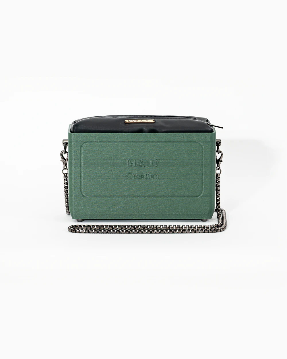Borsa M&IO 01 di tre quarti: scocca ulivi di puglia opaca con la scritta M&IO Creation in rilievo sul fronte, pochette nero che sporge dal bordo superiore, catena in metallo canna di fucile.