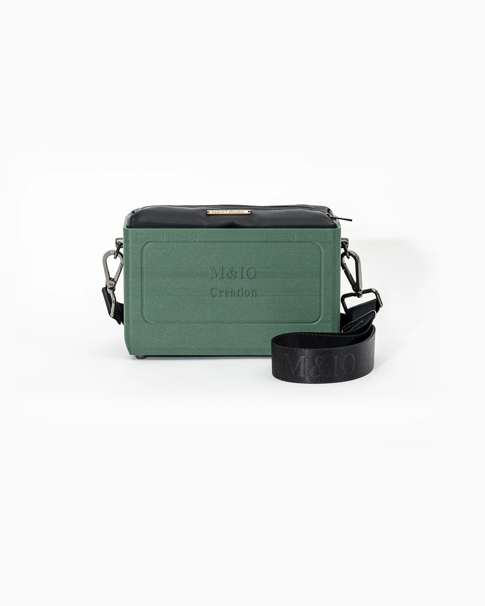 Borsa M&IO 01 di tre quarti: scocca ulivi di puglia opaca con la scritta M&IO Creation in rilievo sul fronte, pochette nero che sporge dal bordo superiore, cinghia in tessuto nero con logo M&IO ripetuto.